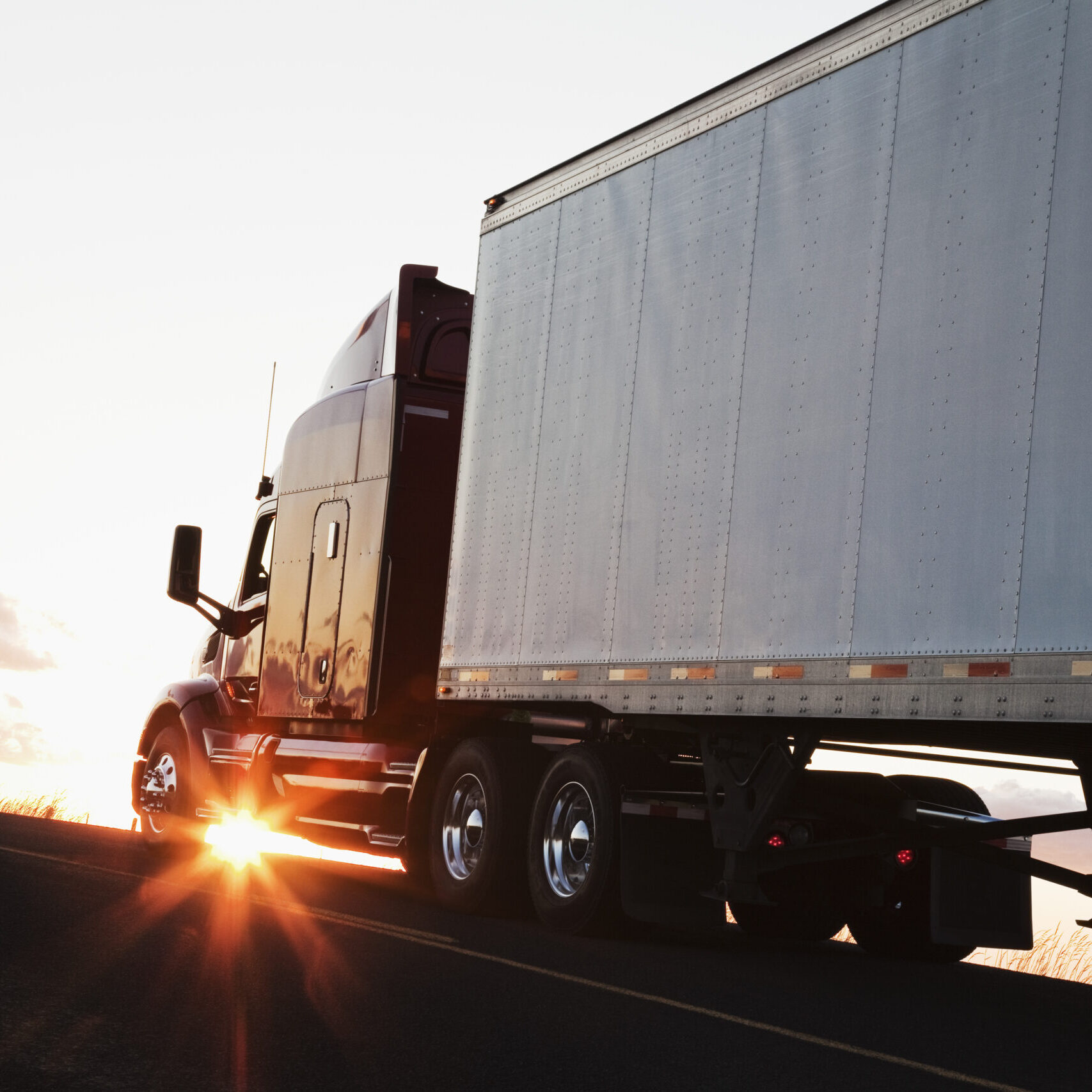 Silhouette of a  commercial truck driving on a highway at sunset.