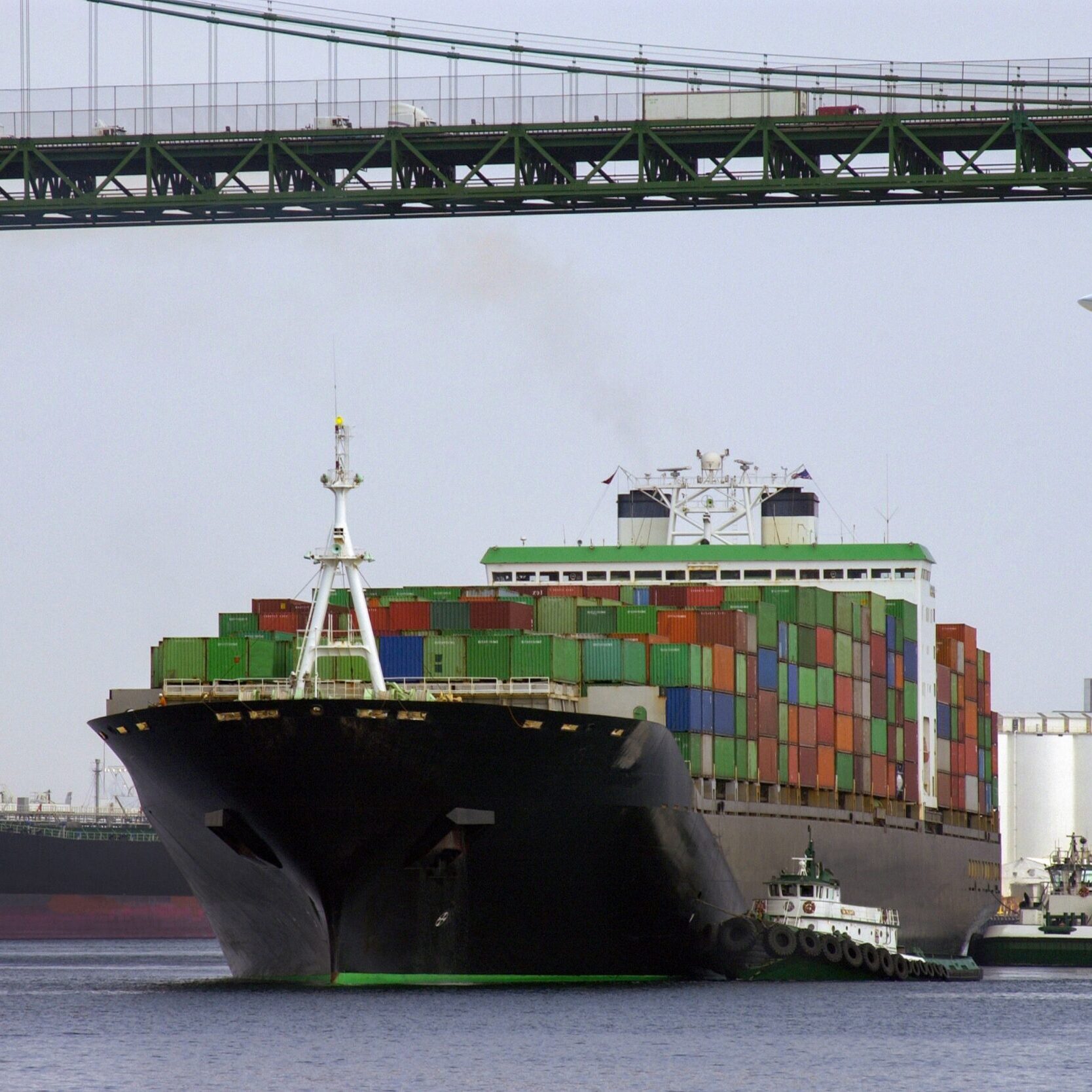 Transport - a large container ship pass under a road bridge with trucks on it with an aircraft coming in to land at a nearby airport.
Port of Long Beach, California, USA.